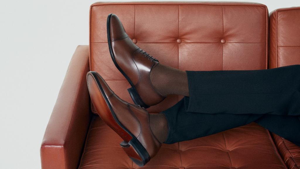 Pessoa sentada com calça escura, meia marrom de cano alto e Oxford Melrose Café.